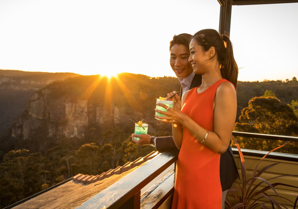 Couple enjoying a drink and views of the sun setting over Blue Mountains National Park from Echoes Boutique Hotel and Restaurant, Katoomba
